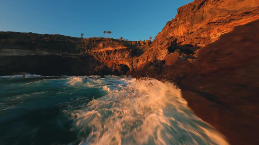 Flying fast over a rocky coast with the sea waves hitting the rocks with force