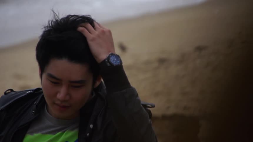 Man puts his hand through his hair as he walks on the beach