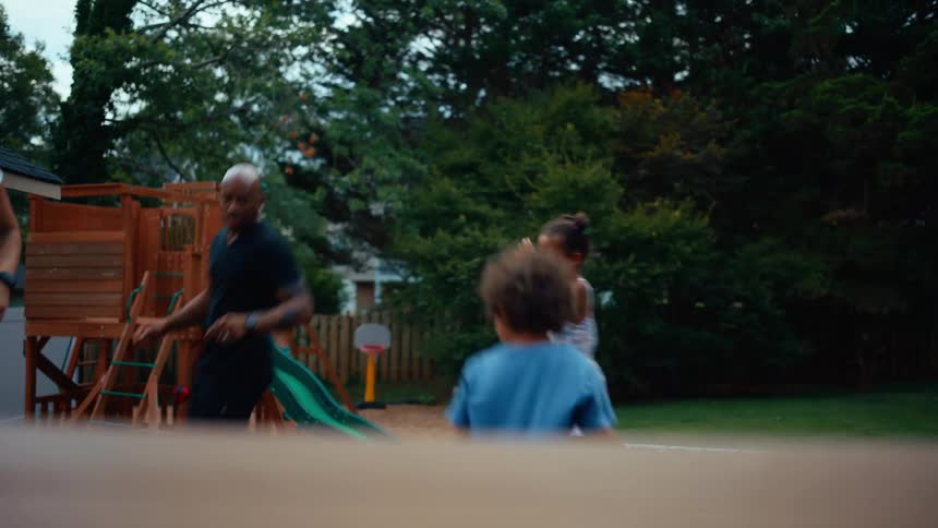 A woman man and child joyfully dance together in a backyard near a wooden playset