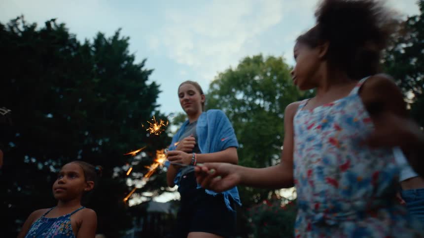 A group of girls holding sparklers in an outdoor setting on a summer day
