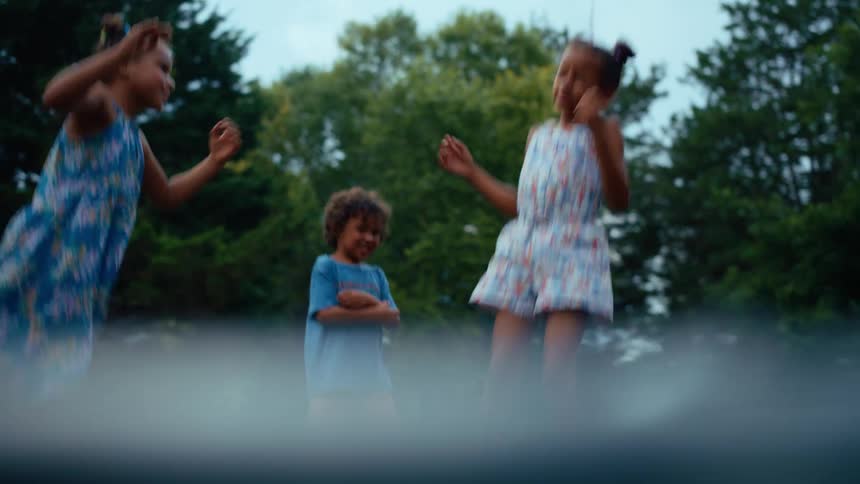 A group of three children jump up and down on a trampoline outdoors