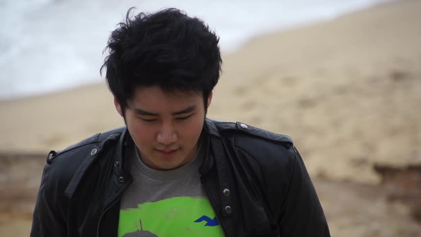 A young, asian man walking away from the water at the beach