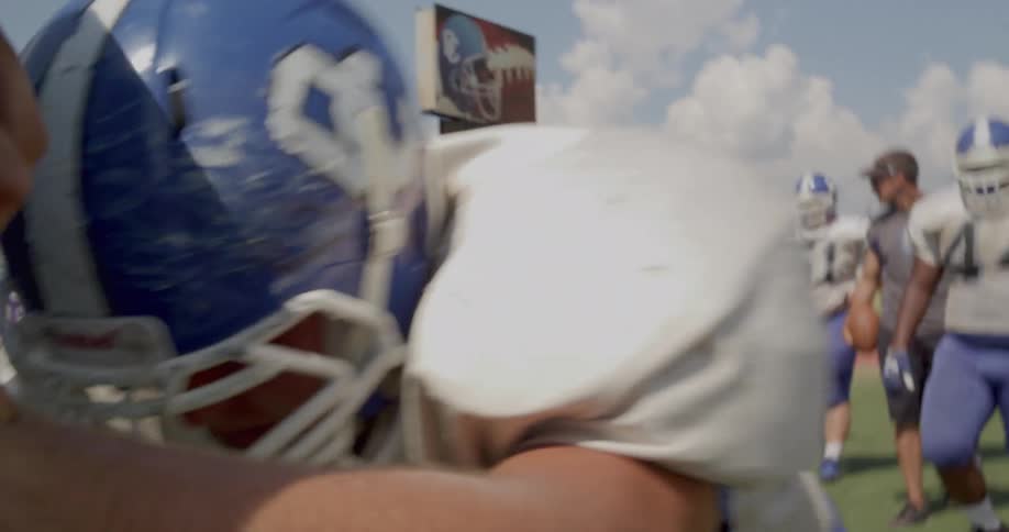 The video shows a football practice with two distinct lines of players in the foreground a player wearing a blue helmet and white jersey with the number 36 is running toward the camera in the background there is a stationary line of players in white j