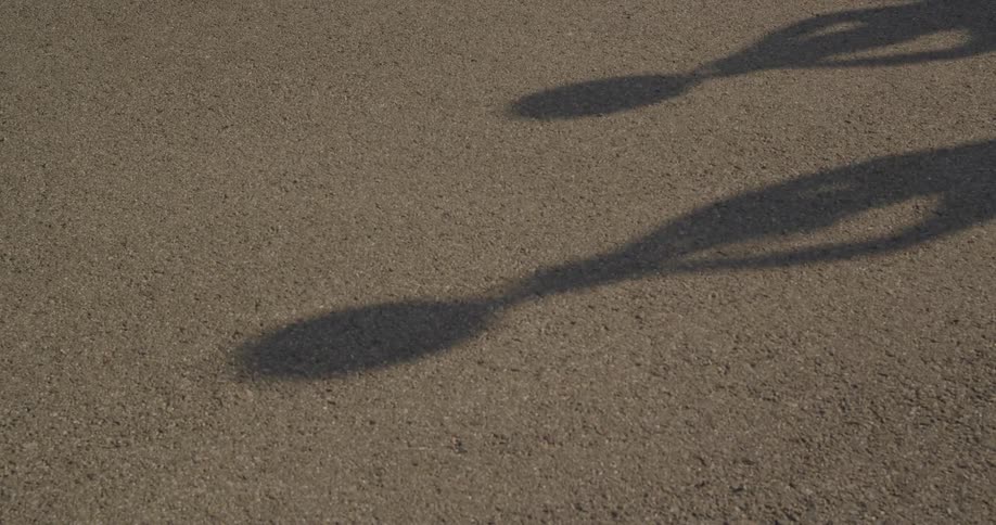 Shadows of people carrying something over their heads during training move across asphalt