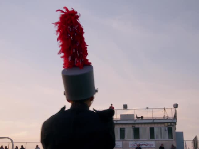 A marching band player with a feathered hat looks toward the stands