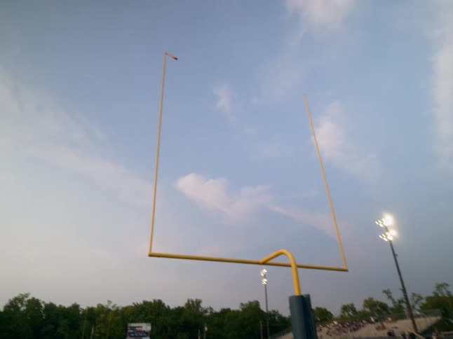 An american college football field with a bright yellow goal post stands under the glow of stadium lights