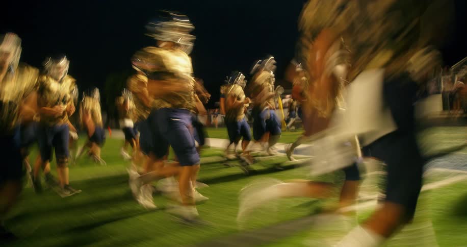 American football team running on a grass field at night