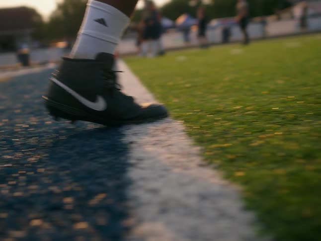 The feet of a teenage boy in cleats walking across a football field