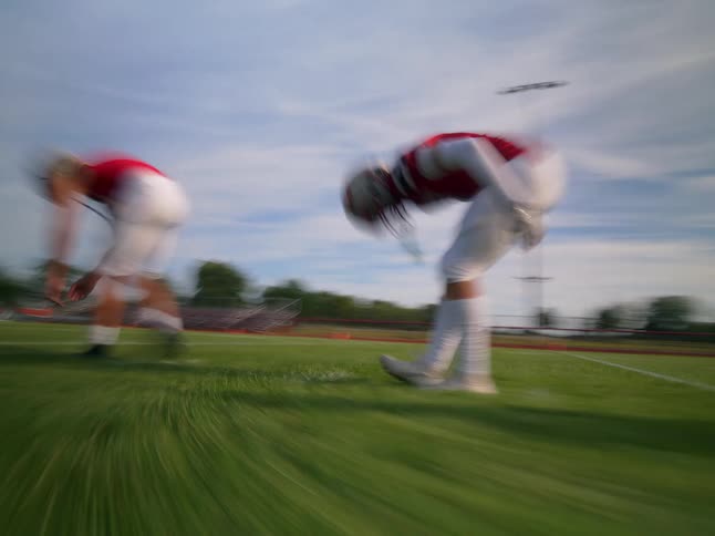 Two football players lean down and stretch while walking across a football field