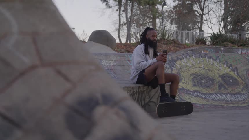 Man interacting with a smartphone while sitting at a skate park