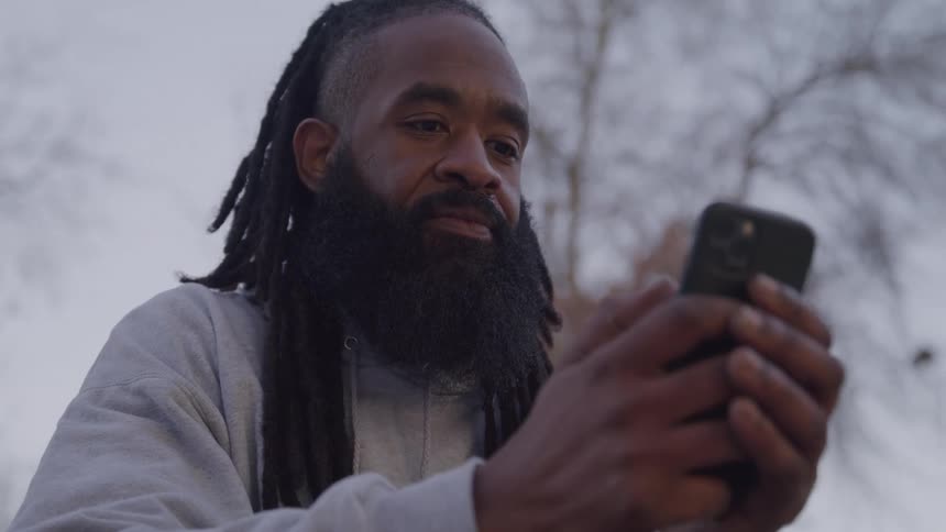 Man outdoors interacting with both hands on a smartphone