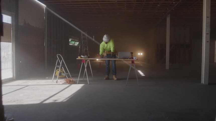 Worker wearing a helmet and reflective vest points while organizing materials on a workbench at the construction site