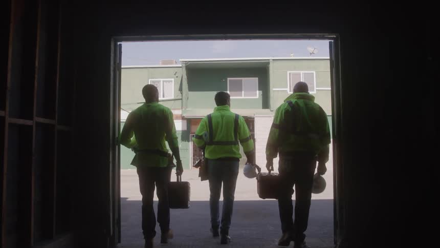 Three men in divisive vests coming out of a warehouse