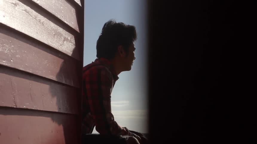 Man sitting by the side of a house on a cloudy day