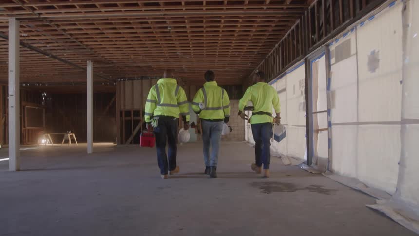 Three workers in reflective vests walk through a building under construction