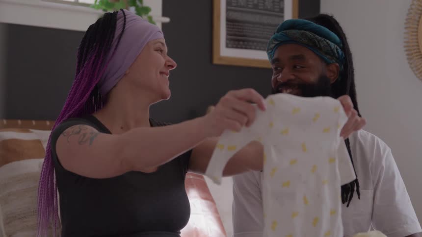 Woman and man smile while examining a baby outfit at home