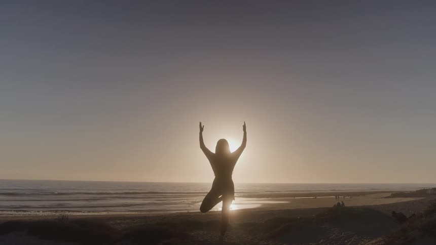 A silhouette of a person on a beach stretches their arms toward the sky as the sun sets behind them the waves gently roll in and out creating a peaceful and inspiring atmosphere