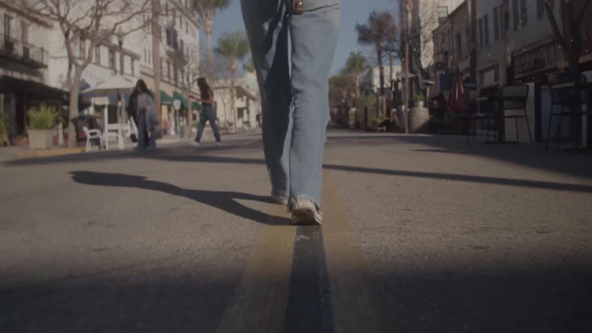 Person walks along the middle of the street between buildings and palm trees