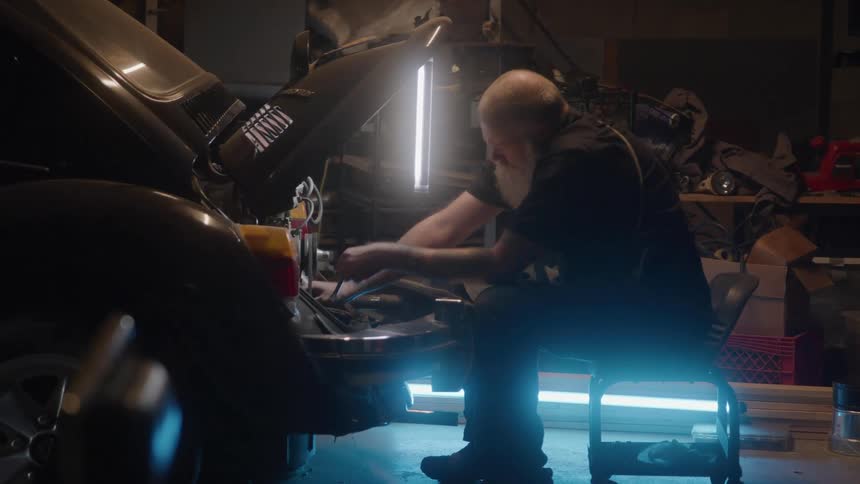Middleaged male mechanic working on the engine of a parked car inside a garage