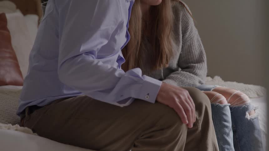 Man comforts woman sitting side by side on the edge of the bed