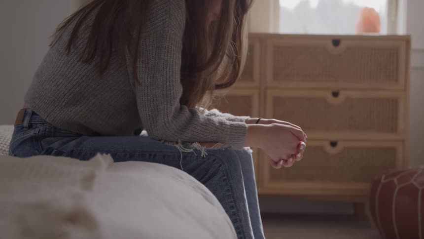 Woman sitting on the edge of the bed with hands clasped