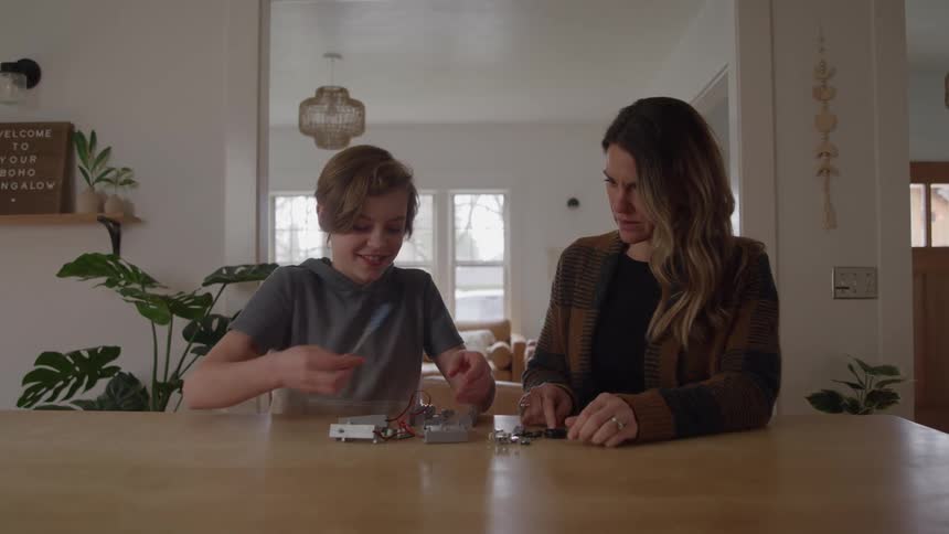 Boy assembles electronic components while the mother watches attentively