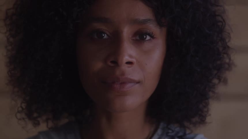 A woman with curly hair looks directly into the camera with a gentle expression