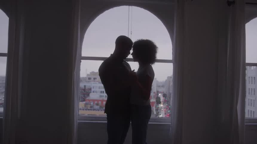 A silhouette of a couple is embracing and looking at each other in a window with a city street visible below