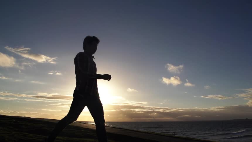 Man walking on the beach as the sun sets behind him