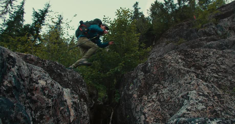 Adventurer with a backpack jumps between rocks in the forest