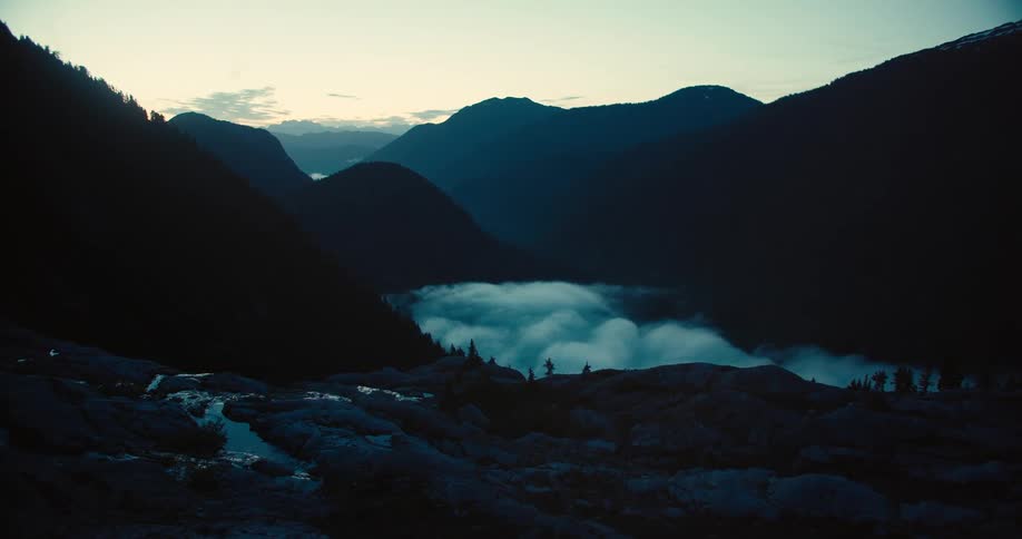 A misty valley lies surrounded by silhouetted mountains at dawn