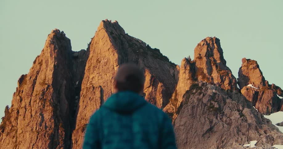 Man stands watching craggy mountains during the daytime