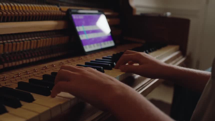 A person plays an open piano using a tablet for guidance