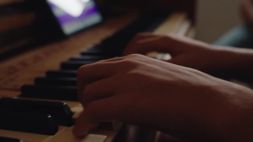 Fingers press the keys of a piano in an indoor setting