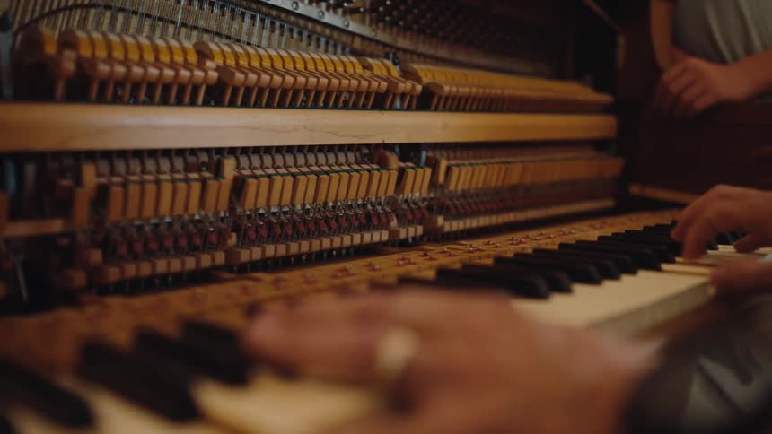 A closeup shot shows the inner mechanics of an upright piano before shifting focus to the musicians hands as they play the keys