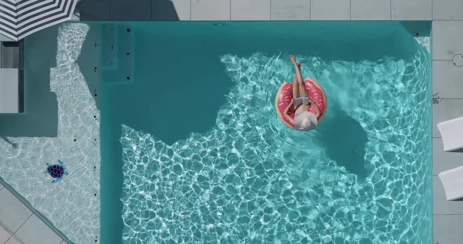 Woman floats in a ring floatin a swimming pool on a summer day while reading a book
