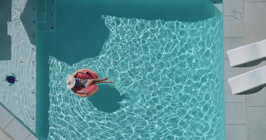Woman lies in a ring float while floating in a swimming pool on a summer day