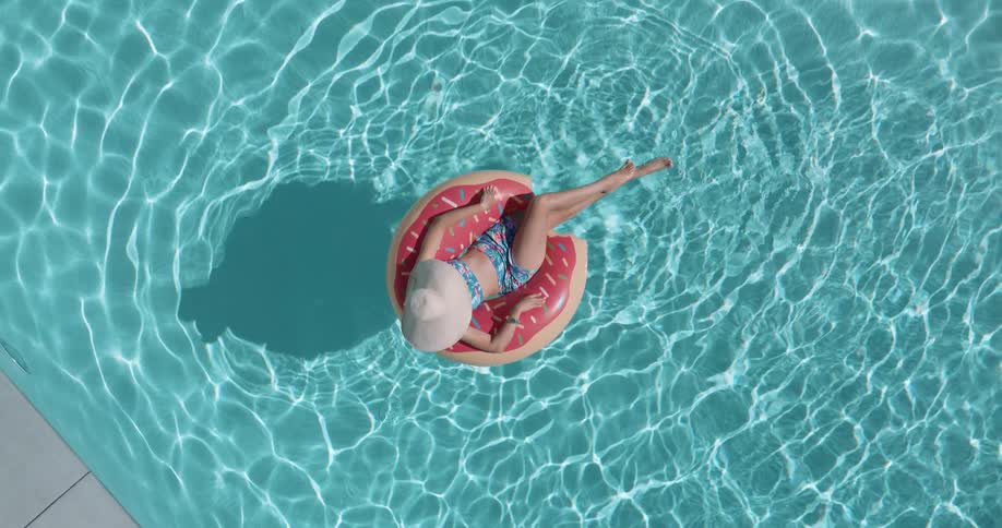 Woman in hat and bikini lying on a donut float in the pool