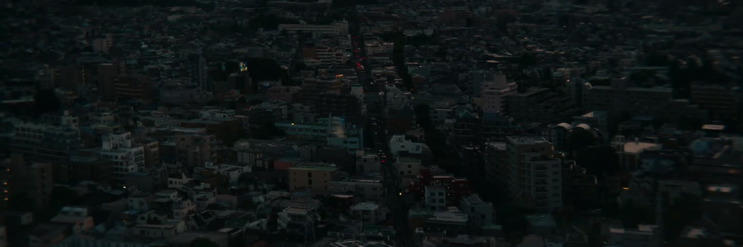 Aerial view of a city shows streets lit by headlights at dusk