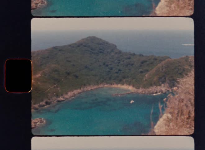 Cinematic Super 8mm panoramic sweep over a twin-cove turquoise bay, showing rocky cliffs, dense green vegetation, a crowded sandy beach and anchored boats below, captured from a high cliff viewpoint in warm vintage analog film style