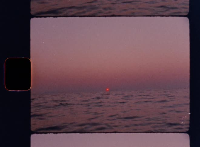 Cinematic Super 8mm sunrise over the calm ocean horizon, with a small glowing red sun emerging through a hazy pink sky and gentle rippling waves, captured in authentic vintage film grain and framed by classic analog film strip borders