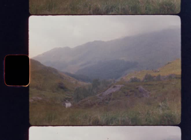 A shot of an old film strip shows a landscape with a river and rolling hills covered in mist the film is in a horizontal strip with two additional blank frames visible
