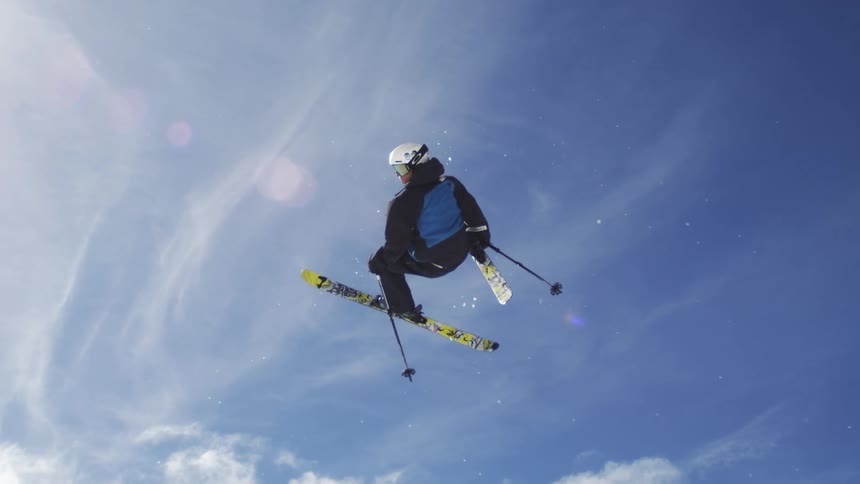 A skier in mid air executes a trick against a bright blue sky with scattered clouds