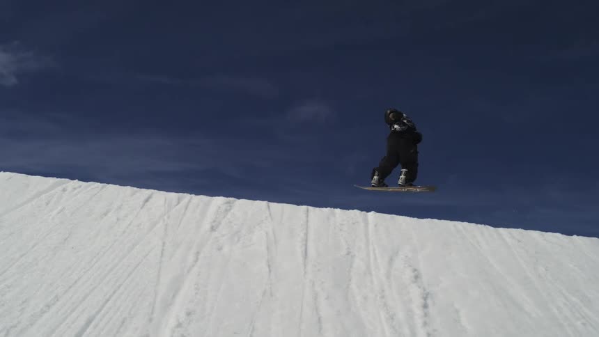 The video shows two shots of a snowboarder in midair on a snowy mountain the first shot is a closeup against a dark blue sky while the second pulls back to show the surrounding snow and ski lifts with a filmsupply watermark visible in the center