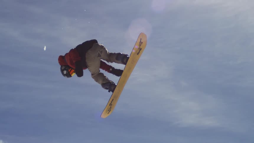 Snowboard rider in full snowboarding gear captured midair on a sunny winter day in the mountains performing an impressive stunt high above the snowy slopes