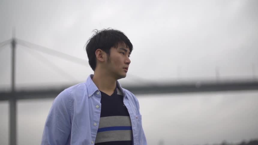 A man stands with a bridge behind him