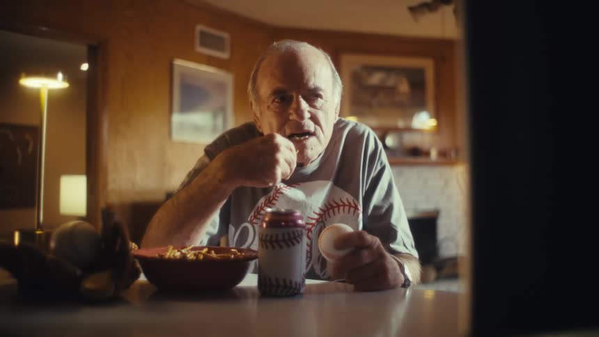 Elderly man in a baseball shirt eating at the table