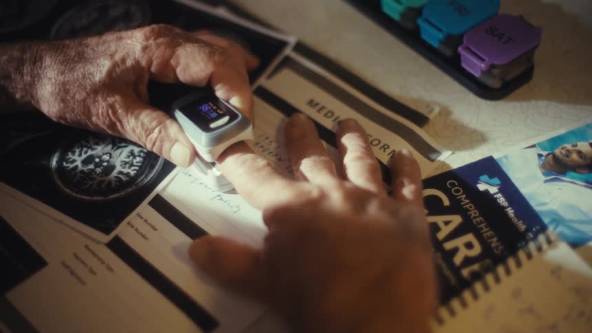 A mans hand is shown in a closeup with a pulse oximeter on his finger next to his hand are documents including a medical form and a brochure for fsp health