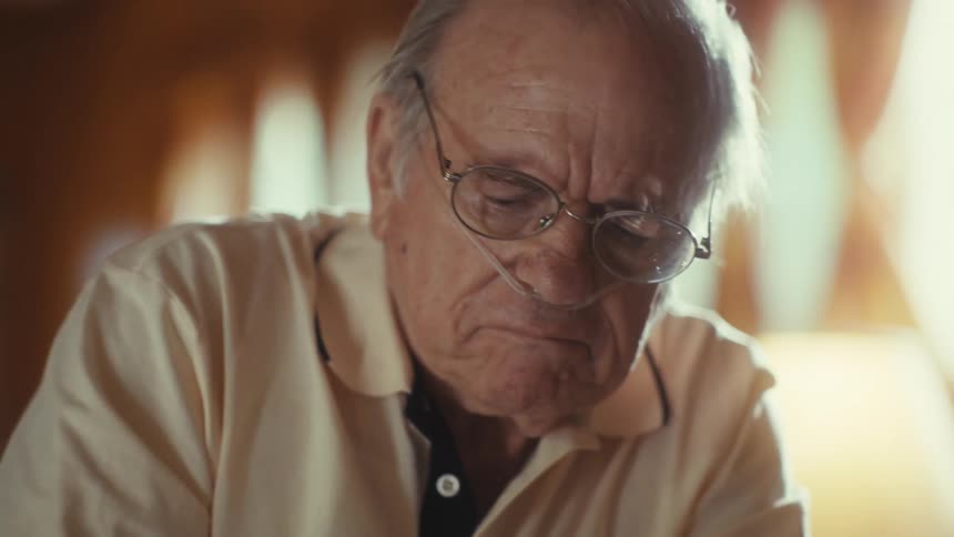 The first shot shows a hand signing a medical form with the forms title medical form in reverse indicating a mirror shot the second shot is a closeup of the elderly man with glasses from the previous video wearing a nasal cannula looking