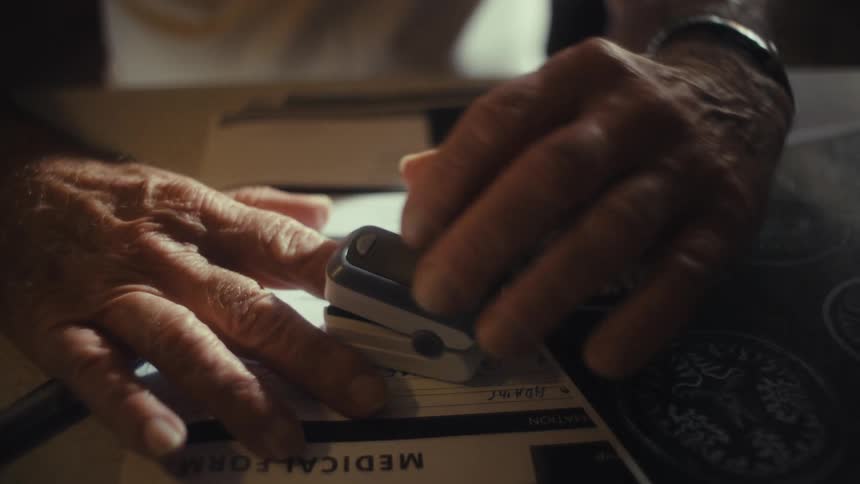 Elderly hands using a fingertip oximeter over medical forms